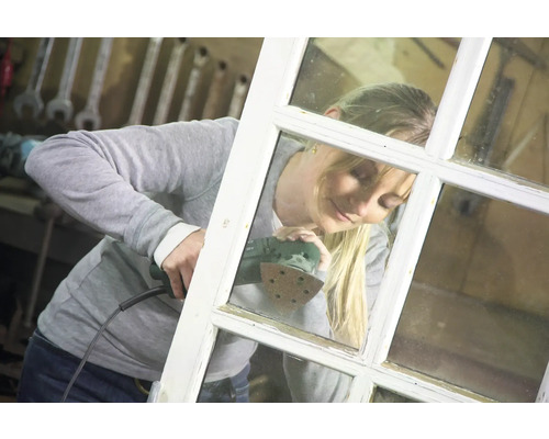Eine Frau schleift einen Fensterrahmen mit einem Schleifgerät