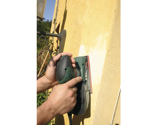 Eine Person verwendet einen Schwingschleifer an einer Wand.