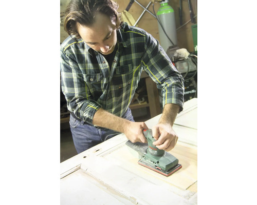 Ein Mann schleift eine Holztür mit einem elektrischen Schleifgerät.