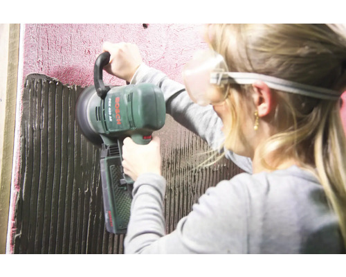 Une personne utilise une carrelette de la marque Bosch pour appliquer de la colle à carrelage.