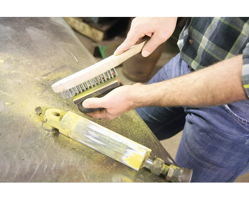 Mann reinigt Metall mit Drahtbürste