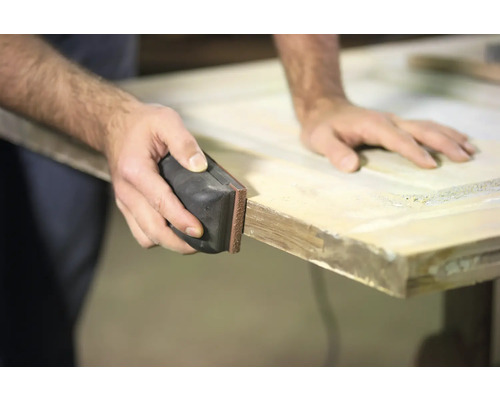 Eine Person schleift eine Holztür mit einem Schleifklotz.