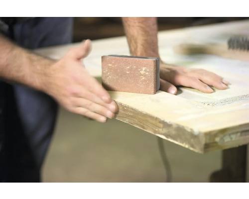 Eine Person schleift eine Holzoberfläche mit einem Schleifklotz.