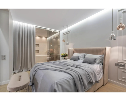 Chambre lumineuse avec lit double, table de chevet et salle de bains attenante derrière une porte coulissante en verre