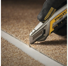 Une personne coupe de la moquette avec un cutter à moquette. Le cutter à moquette est de Stanley.