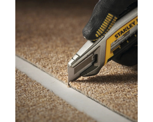 Une personne coupe de la moquette avec un cutter à moquette. Le cutter à moquette est de Stanley.