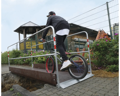 Eine Person fährt mit einem BMX-Rad über eine temporäre Brücke.