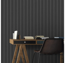 Gros plan d''un bureau avec des livres et une machine à écrire devant un revêtement mural gris avec un motif rayé.