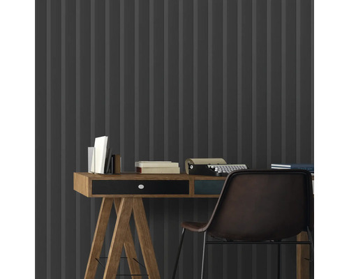 Gros plan d''un bureau avec des livres et une machine à écrire devant un revêtement mural gris avec un motif rayé.