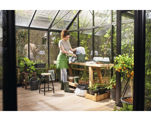 Gewächshausinneneinrichtung mit Frau, die Pflanzen gießt, Tisch, Stuhl und Pflanzen