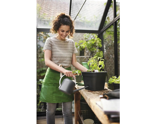 Frau giesst Pflanze in schwarzem Topf mit Giesskanne im Gewächshaus