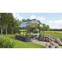 Serre avec cadre en acier, panneaux de verre et fondation sur une pelouse avec mobilier de jardin
