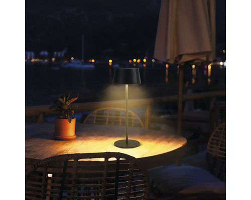 Photo extérieure d''une lampe de table sur une table en bois à l''extérieur la nuit.