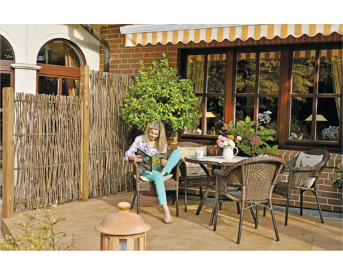 Terrasse mit Sichtschutzzaun, Gartenmöbeln und lesender Frau.