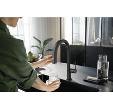 Frau befüllt Glas unter Küchenarmatur mit Wasser