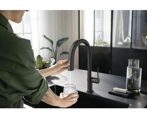 Frau befüllt Glas unter Küchenarmatur mit Wasser