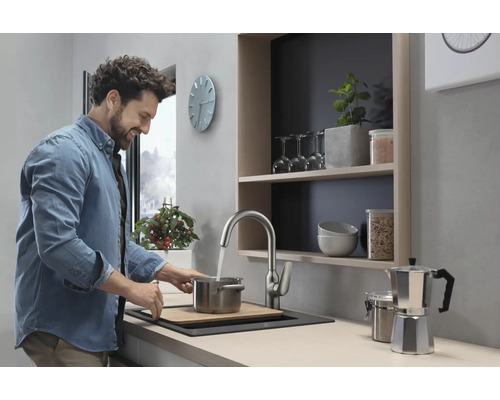 Heller Küchenraum mit Spüle, Wasserhahn und lächelndem Mann beim Kochen