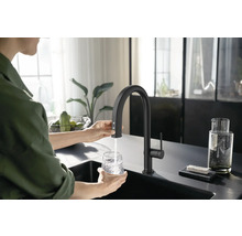 Frau befüllt Glas mit Wasserhahn in einer modernen Küche