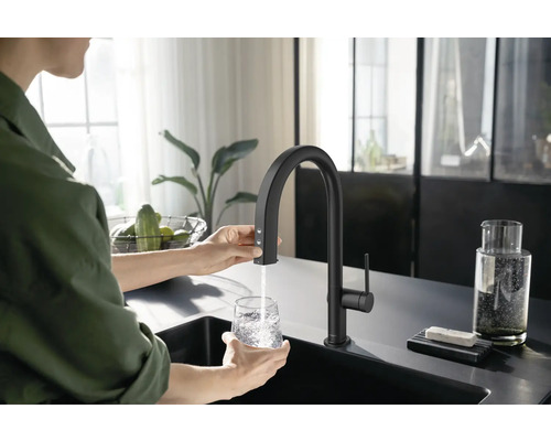 Frau befüllt Glas mit Wasserhahn in einer modernen Küche