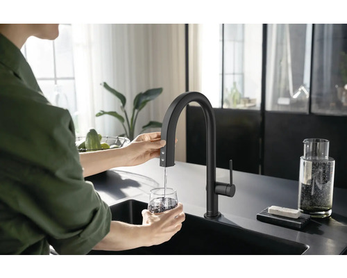 Eine Person füllt ein Glas Wasser mit einer schwarzen Küchenarmatur in einer modernen Küche.