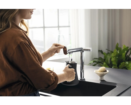 Une femme prépare une boisson avec un robinet et un récipient noir dans l''évier de cuisine.