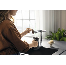 Une femme remplit un récipient noir d''eau provenant d''un robinet de cuisine chromé.