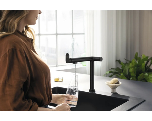 Femme remplissant une bouteille d''eau au robinet de cuisine noir