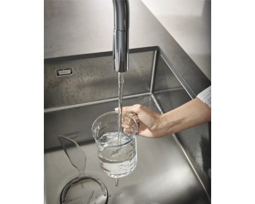 Edelstahlspüle mit Wasserhahn, eine Hand hält ein Messglas unter fließendem Wasser