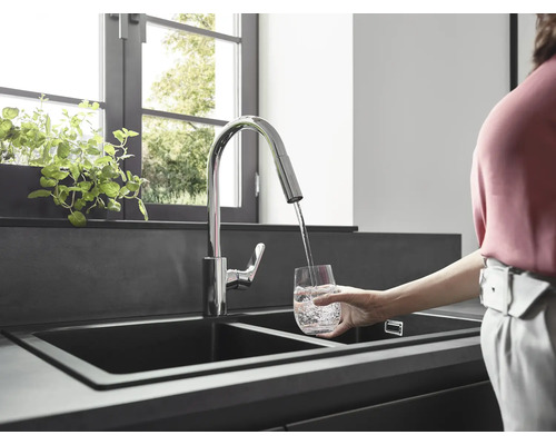 Spültischarmatur mit schwenkbarem Auslauf füllt ein Glas Wasser in einer modernen Küche.