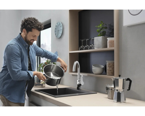 Un homme verse de l''eau d''une casserole dans un évier dans une cuisine moderne.