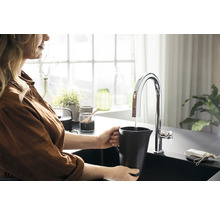 Femme remplissant un pichet noir avec de l''eau d''un robinet dans une cuisine.