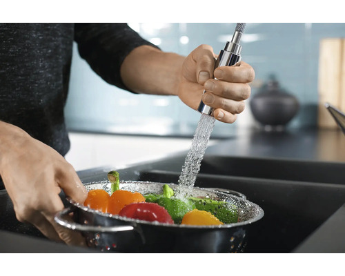 Des légumes sont lavés dans une passoire de cuisine sous un robinet.