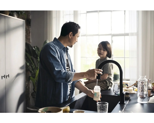 Mann füllt Wasser in eine Babyflasche am Spültisch in der Küche.