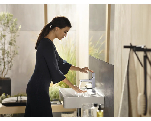 Frau wäscht sich die Hände an einem Waschtisch mit Armatur in einem hellen Badezimmer.