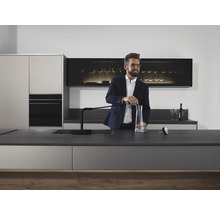 Moderne Küche mit elegantem Design und Mann, der Wasser in eine Karaffe füllt