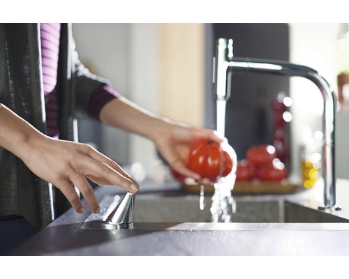 Frau wäscht Tomate unter Küchenarmatur