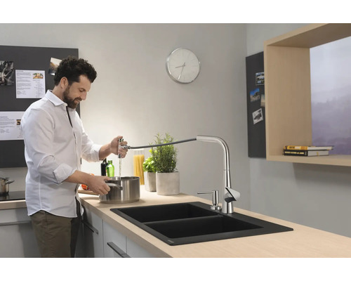 Un homme remplit de l''eau dans un évier de cuisine moderne avec un robinet extractible.