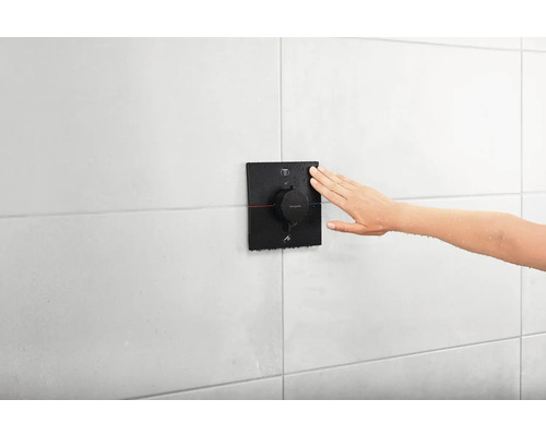 Une main règle un thermostat de douche Hansgrohe sur un mur carrelé