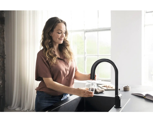 Frau füllt ein Glas Wasser an einer Küchenarmatur