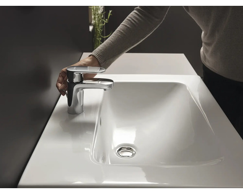 Hand betätigt eine Armatur an einem weißen Waschtisch.