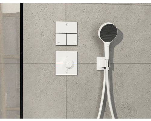 Robinet de douche apparent avec douchette à main devant un mur gris