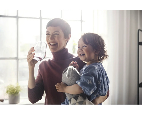 Frau hält Glas Wasser mit Kind im Arm