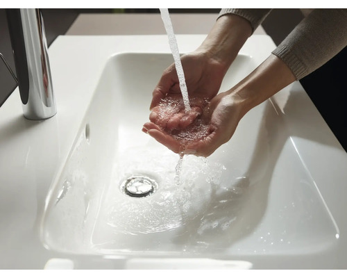 Eine Person wäscht sich die Hände in einem weißen Waschbecken mit einem verchromten Wasserhahn.