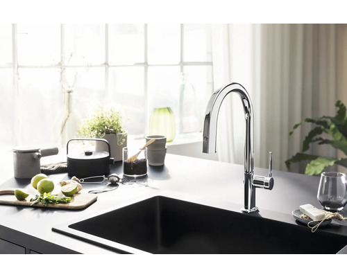 Spültischarmatur aus Metall an schwarzem Spültisch mit Küchenutensilien.