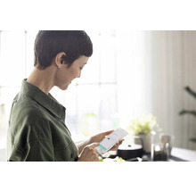 Une femme utilise un smartphone dans une cuisine lumineuse.