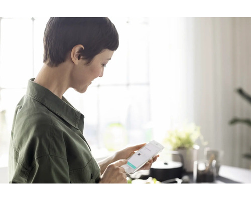 Une femme utilise un smartphone dans une cuisine lumineuse.