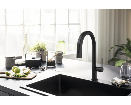 Schwarze Küchenspüle mit Armatur auf einer Küchentheke mit Zitrone, Kräutern und Teeutensilien