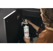 Une femme remplace une cartouche de filtre à eau Hansgrohe sous un lavabo.