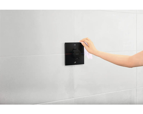 Une main nettoie un robinet thermostatique dans une salle de bain