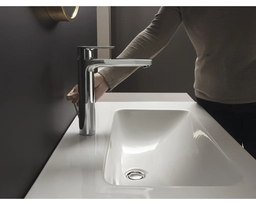 Frau bedient Armatur am Waschbecken im Badezimmer.